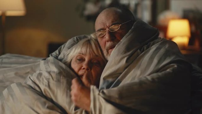 悲伤的老年夫妇在毯子下互相取暖
