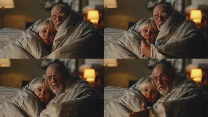 悲伤的老年夫妇在毯子下互相取暖
