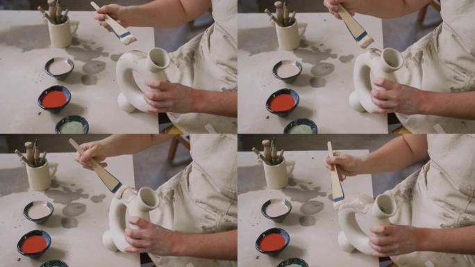 在陶艺工作室，穿着围裙的女性陶艺中段用釉料刷在锅上绘画