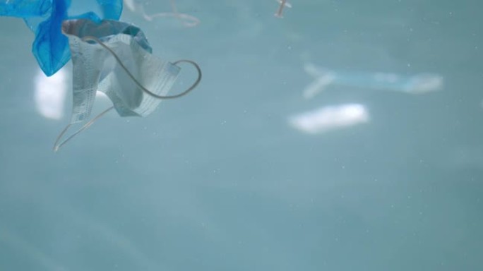 废弃一次性医用口罩在水下。大流行慢动作后，漂浮在海洋中的塑料废物受到污染。