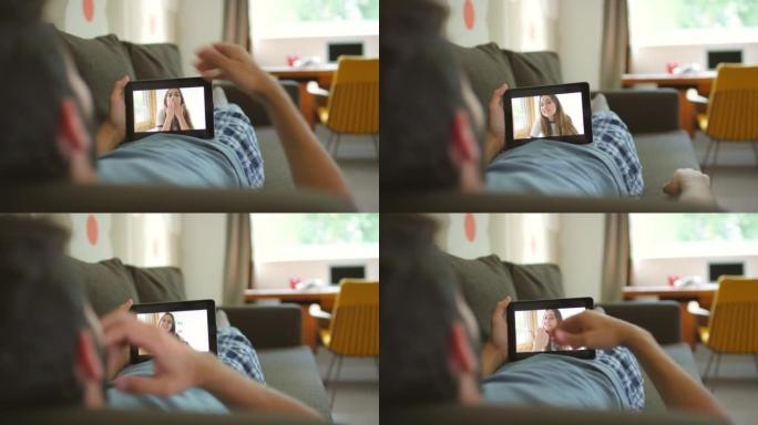 4k视频片段，一名男子使用数字平板电脑在沙发上放松，进行视频通话