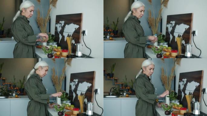 成熟的女士在家里的厨房里准备有机成分的蔬菜沙拉