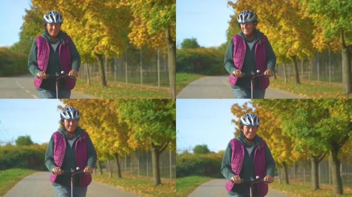 特写: 微笑的老太太在美丽的秋天骑着电动踏板车