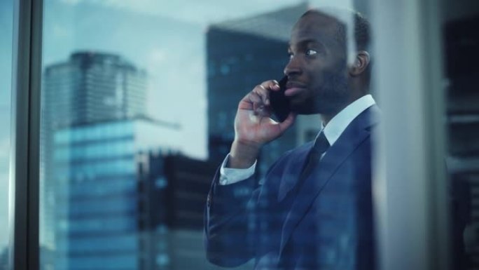 成功的黑人商人站在办公室，打电话完成交易，看着窗外的肖像。成功的电子商务公司董事谈判创业购买。