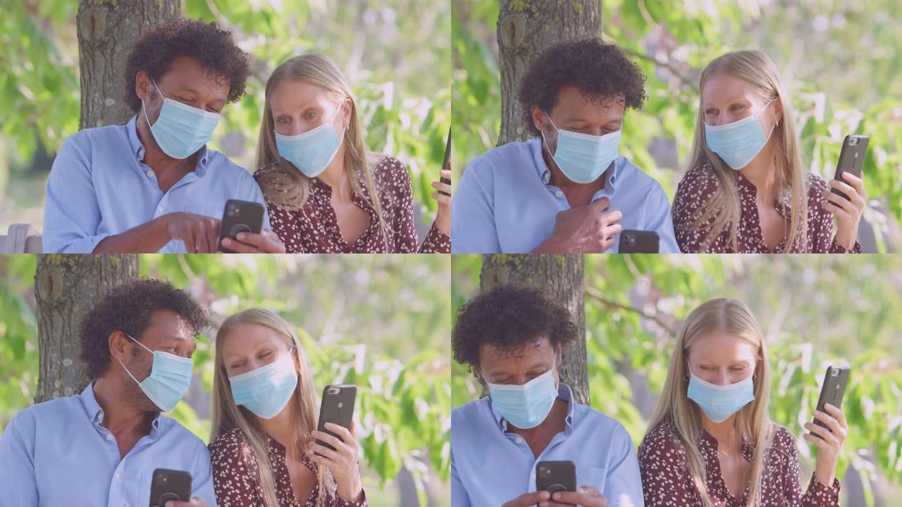 健康大流行期间戴着口罩的夫妇在户外公园见面看手机