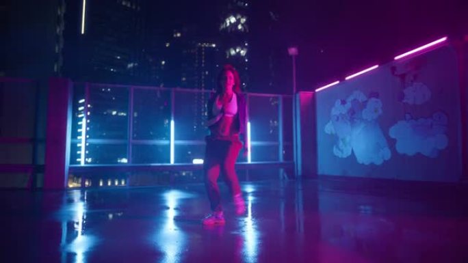 穿着休闲运动服的职业年轻成年女子的肖像在夜晚有摩天大楼的城市中，在霓虹灯的城市街道停车场上积极跳舞
