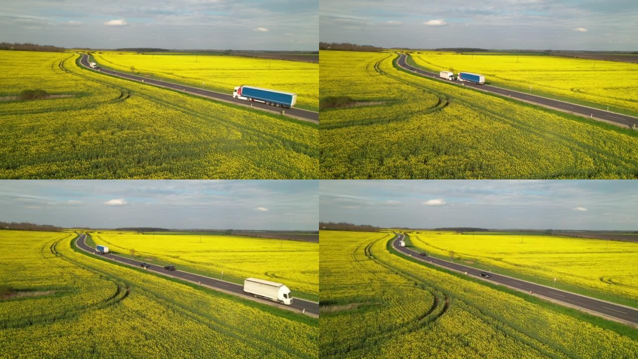 空中: 货车和汽车在高速公路上行驶，经过黄色田野