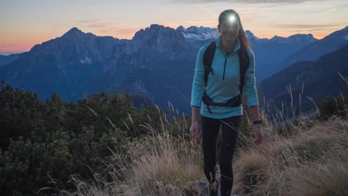 黄昏时分，女徒步旅行者带着头灯在落基山小径上行走