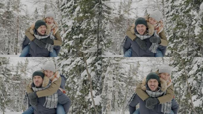 快乐男人的慢动作肖像与女友在冬天在森林里奔跑的女人玩耍