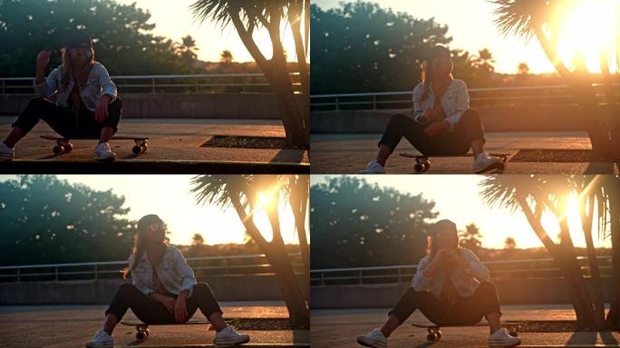 年轻女子，棕色头发，戴着帽子和牛仔夹克，在日落时坐在木板路上的滑板上微笑