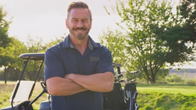 微笑的成熟男性高尔夫球手站在高尔夫球场上的童车旁边的肖像