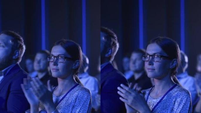 垂直屏幕: 年轻女性坐在科学会议上拥挤的观众中。代表在一次鼓舞人心的主题演讲后欢呼鼓掌。礼堂与年轻成