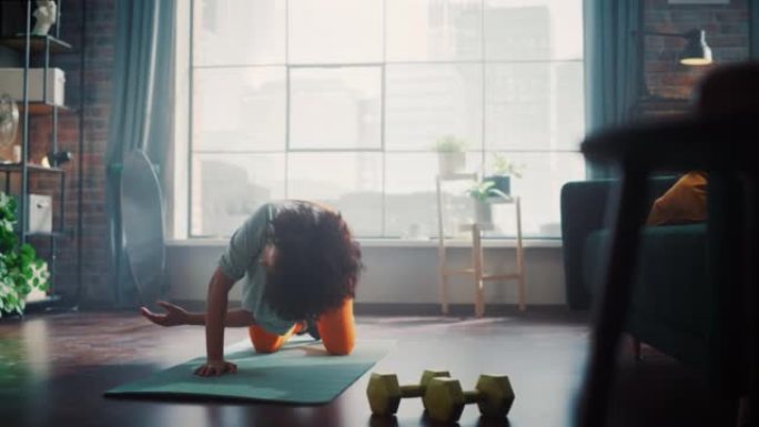 穿着运动运动服的坚强自信美丽的健身女孩正在她明亮宽敞的公寓里做锻炼。集中黑人妇女在瑜伽垫上训练