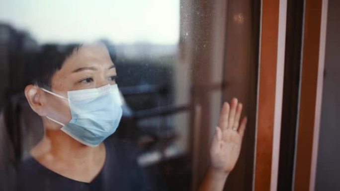 在马来西亚，一名亚洲华裔女性戴着口罩从阳台窗户往外看