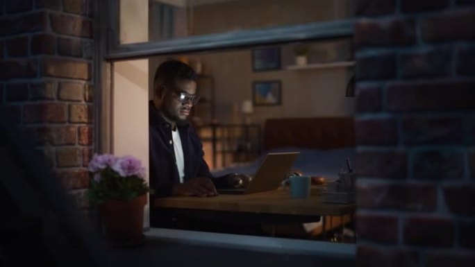 专注的非洲裔美国人在笔记本电脑上在家工作，晚上工作效率高的肖像。专用黑男Web开发人员优化SAAS系