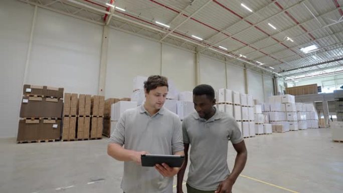 两名持数码平板电脑的男性工人在仓库里行走和讨论