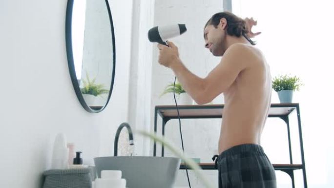 好看的混血男子在浴室用电动吹风机吹干头发的侧视图