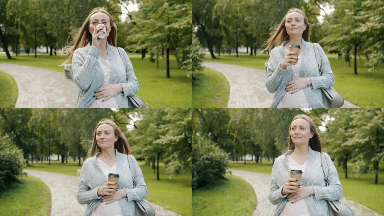 多莉拍摄迷人的孕妇在夏季公园散步喝酒带走咖啡微笑享受大自然