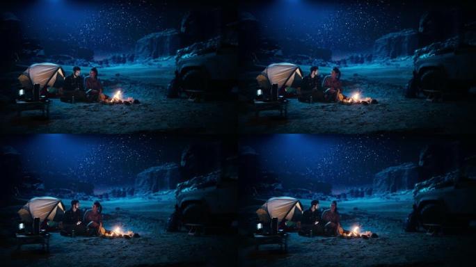 快乐的情侣晚上在峡谷露营，使用数字平板电脑，坐在篝火旁。两个人玩得开心，微笑，在社交媒体上发布旅行照
