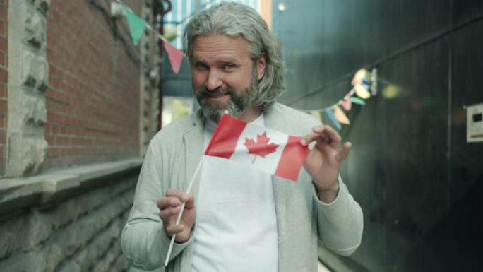 快乐的成熟男人的肖像，举着加拿大国旗站在街上微笑着看着相机