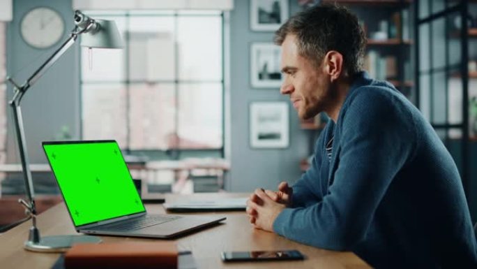 英俊的高加索专家在笔记本电脑上通过视频通话聊天，并在家庭客厅显示绿屏模型。自由职业者在社交网络上通过