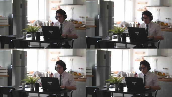 一名亚裔中国年轻人打着领带，穿着长袖衬衫和短裤，坐在餐厅里用笔记本电脑与他的商业伙伴和同事进行虚拟商