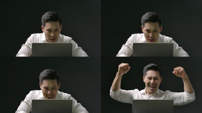 年轻的亚洲人看着笔记本电脑激动的情绪。一个帅哥在网上庆祝工作或学习的成功时刻。在隔离期间，穿着白衬衫