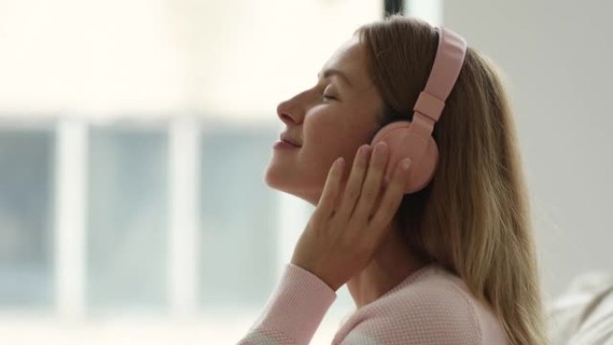 幸福宁静的女人闭着眼睛触摸粉色无线耳机