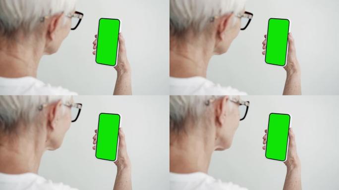 老年人使用带有绿屏色度键特写的智能手机。老女性手持手机模型。概念观看和显示互联网社交媒体，视频通话，