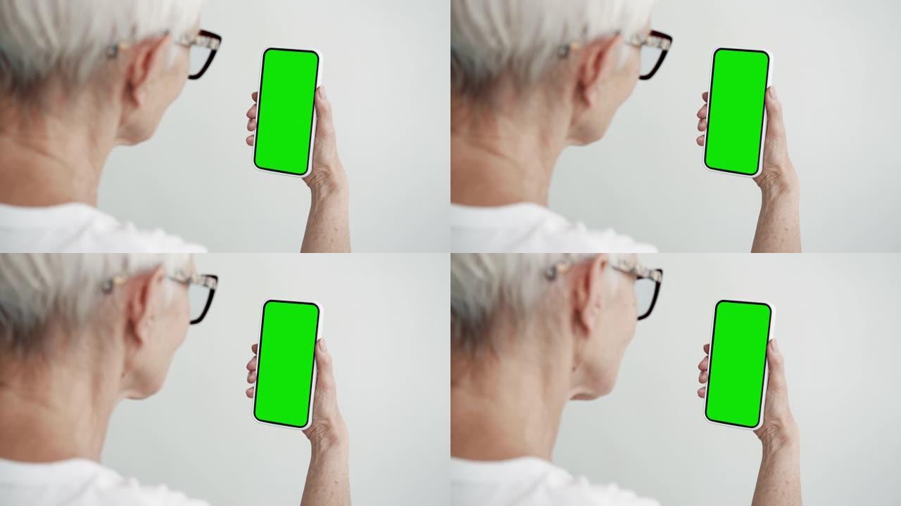 老年人使用带有绿屏色度键特写的智能手机。老女性手持手机模型。概念观看和显示互联网社交媒体，视频通话，