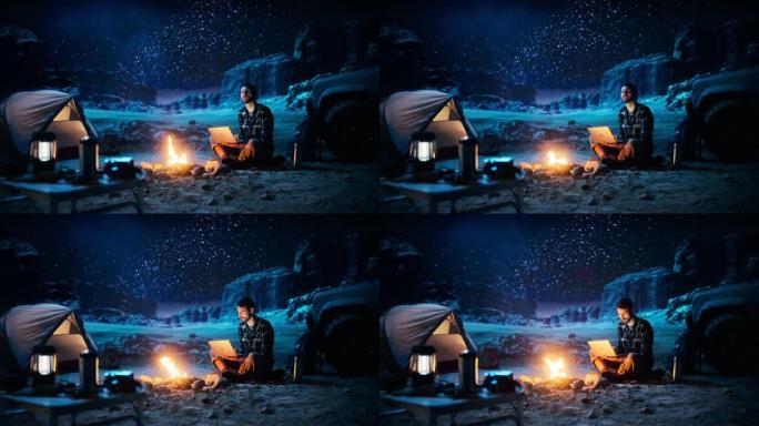 坐在篝火旁的男性旅行者在峡谷中露营时使用笔记本电脑。在度假旅行时通过互联网进行数字远程工作，电子商务