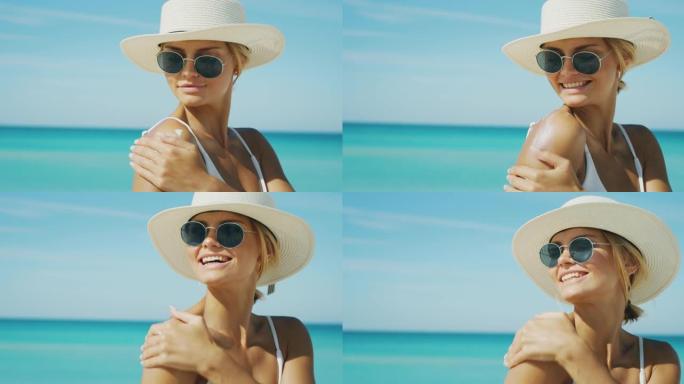 戴着帽子和太阳镜的快乐年轻金发女人的慢动作正在使用防晒霜或晒黑乳液来照顾她的皮肤在海滩度假期间，并在