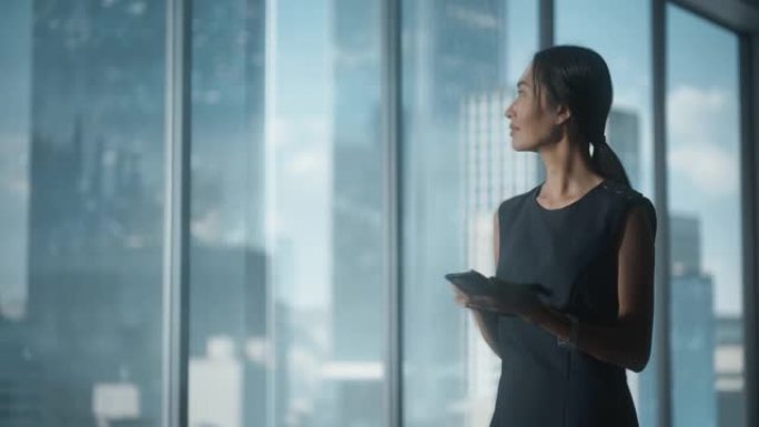 成功的女商人穿着时髦的衣服走在现代办公室，使用智能手机，看着窗外的大城市的摩天大楼。自信的从事金融项