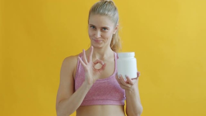 年轻女子的肖像拿着白色的运动补品罐，并表现出ok的手势