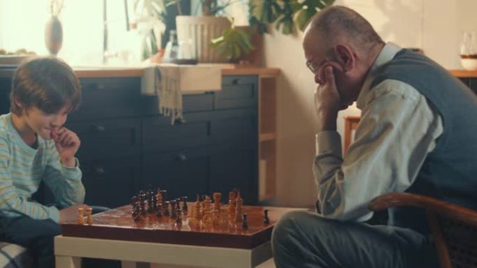 快乐可爱的孩子男孩思考，在老式棋盘上与70多岁的老祖父在家里下棋。