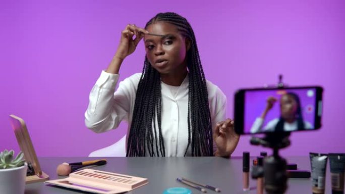 一位年轻的黑皮肤妇女展示了她的化妆配件，并解释了如何使用它们。