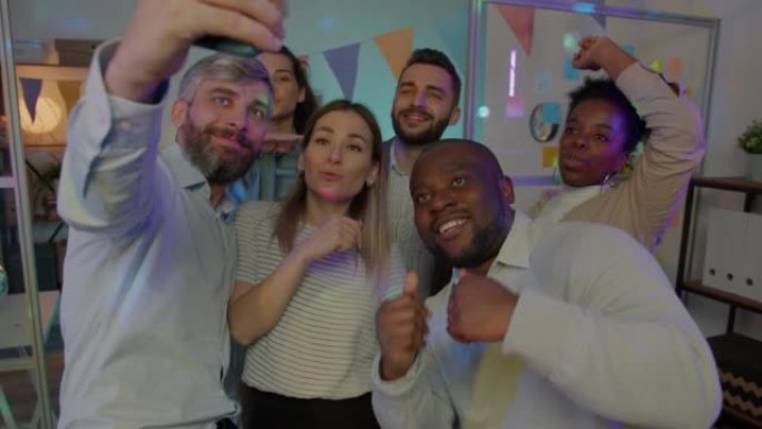 快乐的商人录制了与同事跳舞并为智能手机摄像头摆姿势的办公室聚会视频