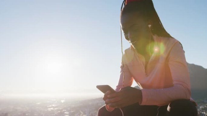 快乐的非洲裔美国妇女在日落时在乡村使用智能手机在户外锻炼