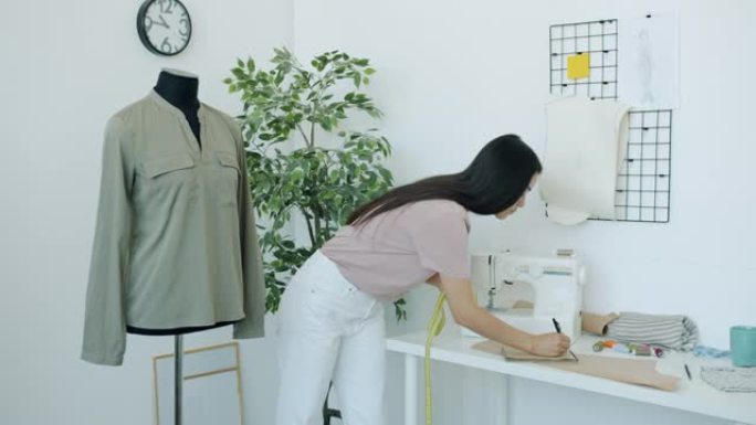 严肃的亚洲时装设计师在工作室忙于创意工作的裁缝假人上测量服装