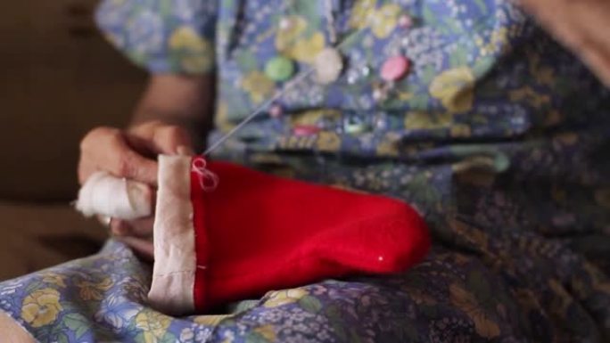 一位老年妇女在家里缝制圣诞老人帽子的皱巴巴的手。特写。