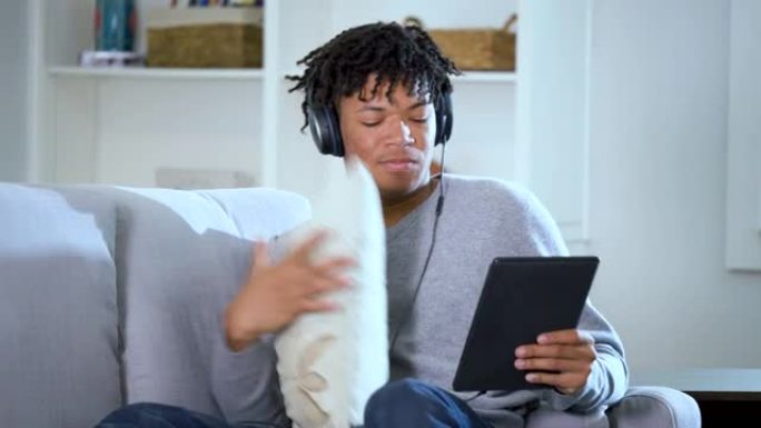 戴着耳机的年轻黑人在沙发上使用数字平板电脑