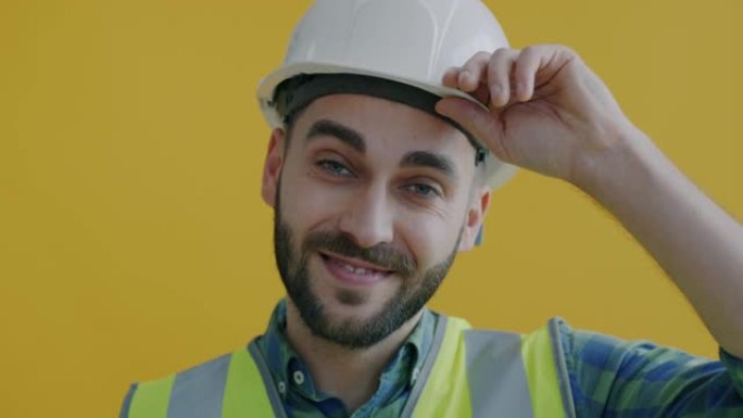 穿着制服触摸安全帽和黄色背景微笑的开朗建筑工人的特写肖像