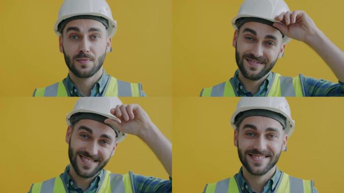 穿着制服触摸安全帽和黄色背景微笑的开朗建筑工人的特写肖像