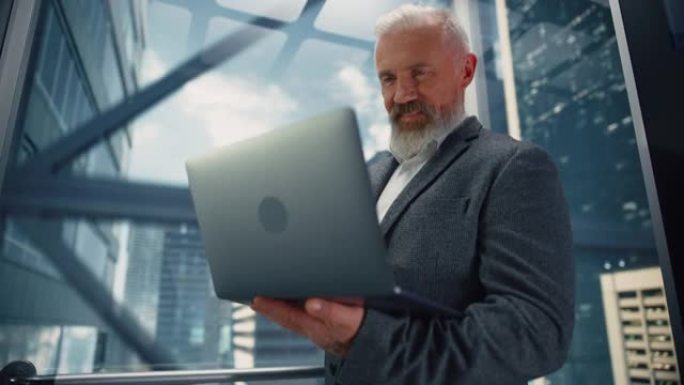 成功的中年商人在现代商务中心乘坐玻璃电梯到办公室。英俊的快乐男人使用笔记本电脑，检查时间表，社交媒体