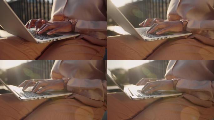 一个皮肤黝黑的女人的手在傍晚的阳光下在笔记本电脑上打字的特写镜头