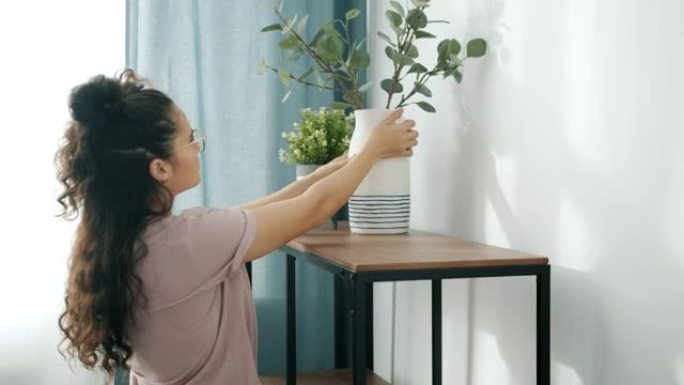 年轻女子用鲜花装饰房屋，将植物放在花盆中，花瓶放在架子上