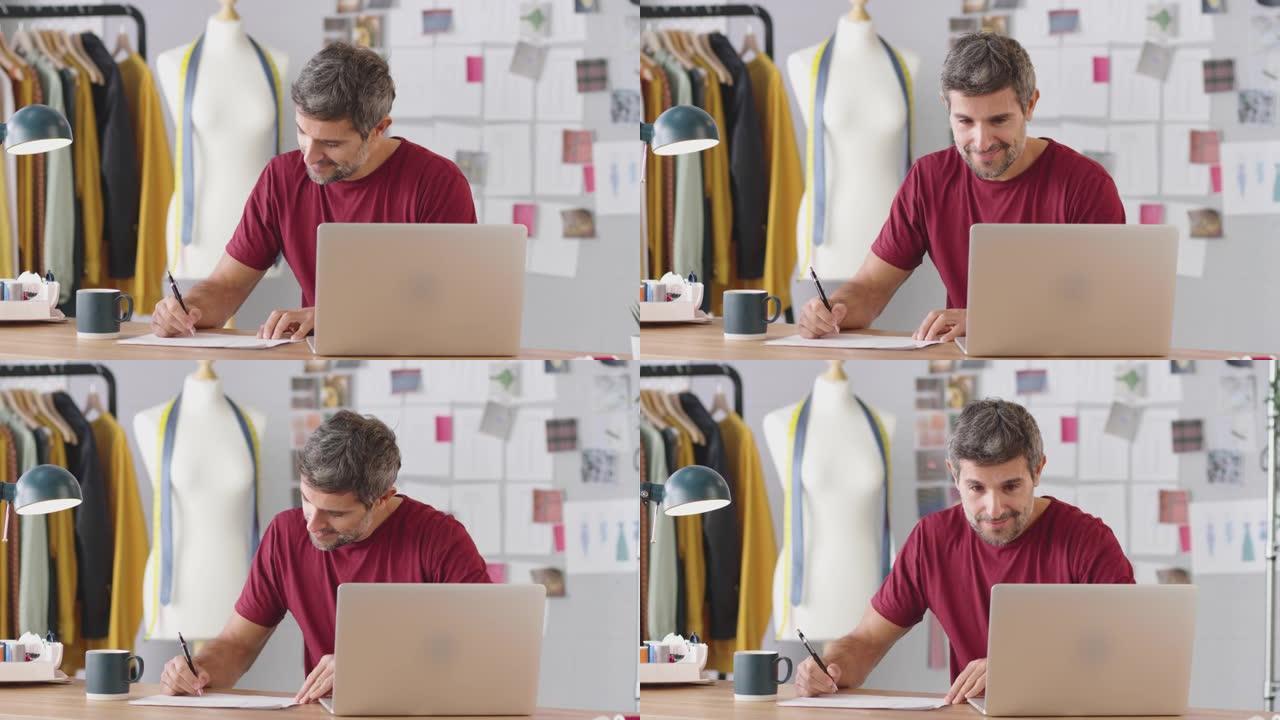 工作室里成熟的男性时装设计师在笔记本电脑上工作