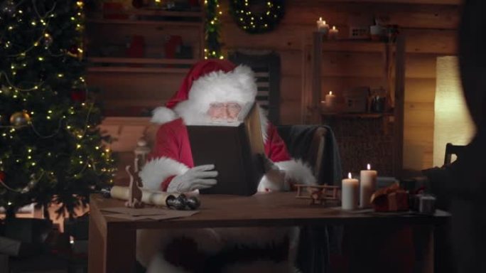 圣诞老人打开他的魔法书坐在蜡烛点燃的黑暗书房里，我们看到魔法光是如何从书中发出的，照亮了圣诞老人的脸