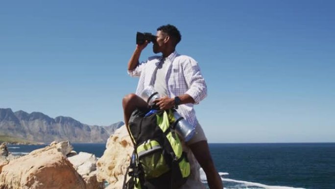非裔美国人使用坐在海岸岩石上的binocilars徒步旅行