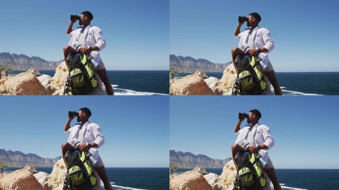 非裔美国人使用坐在海岸岩石上的binocilars徒步旅行